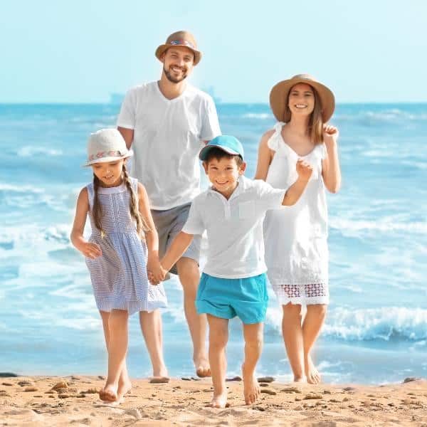 A father, mother, son, and daughter walking together on a sandy beach by the water.