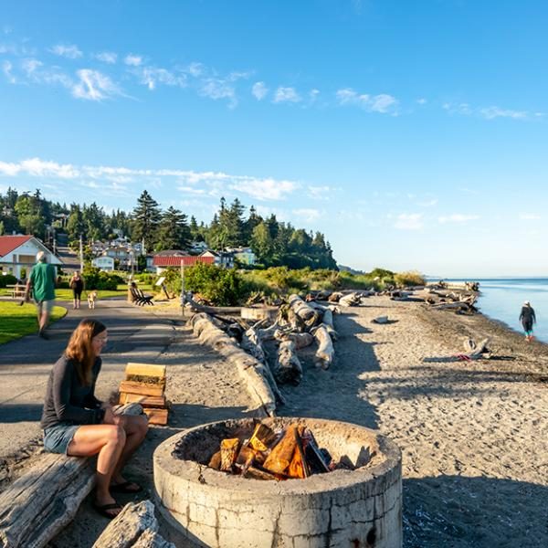 A woman at Mukilteo Lighthouse Park, sitting by a fire pit and looking out at the water.