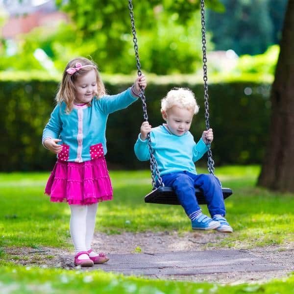 A young girl pushing her brother on a swing set.